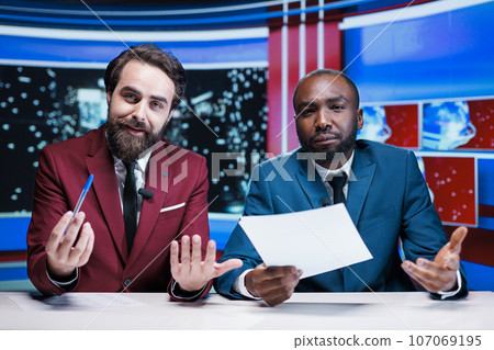 Newscasters reporting breaking news live on television night show, broadcasting global events with relevant information. Diverse team of presenters working in television media industry. 107069195