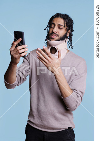 Arab patient with cervical collar having online consultation with doctor on smartphone. Man wearing neck brace talking with general practitioner on smartphone about trauma Arab patient with cervical collar having online consultation with doctor on smartphone. Man wearing neck brace talking with general practitioner on smartphone about trauma 107069228