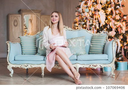 Happy cheerful model woman sitting on blue sofa at home, holding present gift box.  107069406
