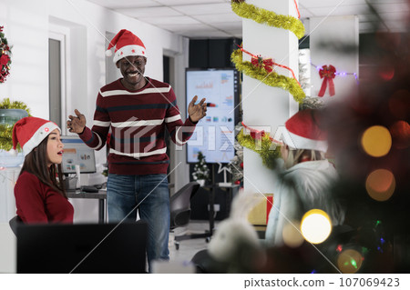 Diverse business team enjoying coffee break at work, having fun together in festive adorn office during holiday season. Colleagues feeling Christmas spirit mood, relaxing in xmas ornate workspace 107069423