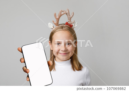 Portrait of happy Xmas girl holding smartphone with empty white screen display. Christmas concept Portrait of happy Xmas girl holding smartphone with empty white screen display. Christmas concept 107069862