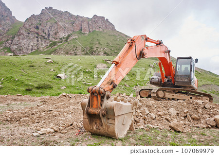 Excavator works in the highlands. Clears the consequences of a mudslide in the gorge of the mountains. repair and expansion of a road Excavator works in the highlands. Clears the consequences of a mudslide in the gorge of the mountains. repair and expansion of a road 107069979