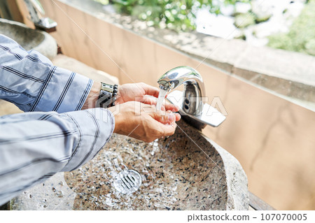 A man's hand touches the water in a beautiful sink with a metal faucet next to an mirror. Close-up of an elegant faucet in the bathroom sink next to stylish decorations. A man's hand touches the water in a beautiful sink with a metal faucet next to an mirror. Close-up of an elegant faucet in the bathroom sink next to stylish decorations. 107070005