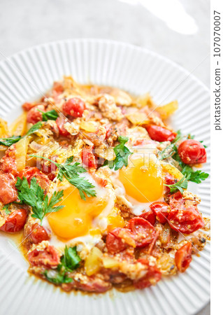 Shakshouka for breakfast. Homemade shakshuka, fried eggs, onion, bell pepper, tomatoes and parsley in a pan. Marble background. Top view. chakchouka Shakshouka for breakfast. Homemade shakshuka, fried eggs, onion, bell pepper, tomatoes and parsley in a pan. Marble background. Top view. chakchouka 107070007