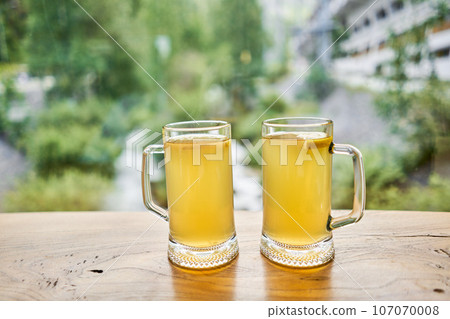 Cup of ginger root tea with lemon, honey and mint on a wooden table and High-mountain river in the background. Walk in the mountains and relax in a cozy cafe. Hiking on a day off Cup of ginger root tea with lemon, honey and mint on a wooden table and High-mountain river in the background. Walk in the mountains and relax in a cozy cafe. Hiking on a day off 107070008