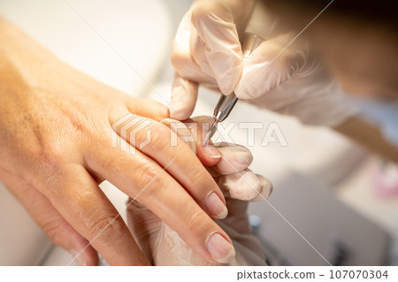 Nail care procedure in a beauty salon. Female hands and tools for manicure, process of performing manicure in beauty salon. Gloved hands of a skilled manicurist cutting cuticles. Concept spa body care Nail care procedure in a beauty salon. Female hands and tools for manicure, process of performing manicure in beauty salon. Gloved hands of a skilled manicurist cutting cuticles. Concept spa body care 107070304