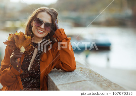 smiling young woman in orange trench coat 107070355