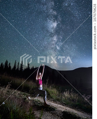 Sporty girl doing yoga pose in moutains on background of Milky Way. Young girl doing yoga under starry sky. Gymnastic exercises in night mountains. Sporty girl doing yoga pose in moutains on background of Milky Way. Young girl doing yoga under starry sky. Gymnastic exercises in night mountains. 107070628