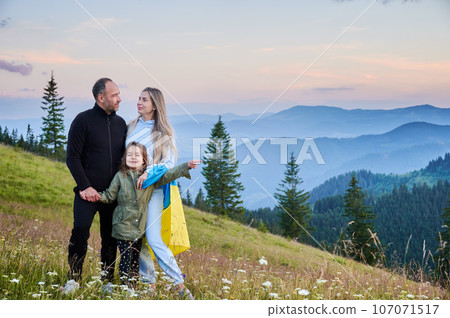 Lovely Ukrainian family resting in mountains. Male adult and his wife standing with their child that pointing at something. Carpathian mountains landscape. Lovely Ukrainian family resting in mountains. Male adult and his wife standing with their child that pointing at something. Carpathian mountains landscape. 107071517