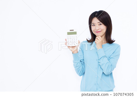 A woman in her 30s holding a calculator and thinking in front of a white background A woman in her 30s holding a calculator and thinking in front of a white background 107074305