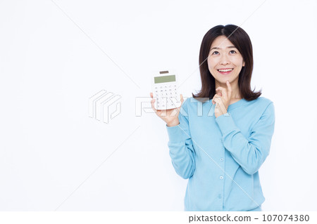 一名 30 多歲的女性拿著計算器，在白色背景前微笑著思考 107074380