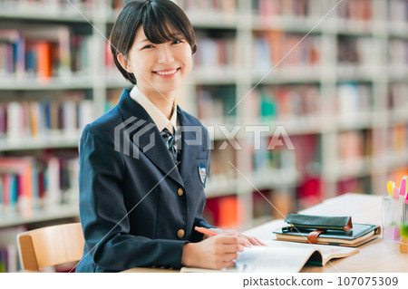 High school girl smiling while spreading out materials in the library 107075309