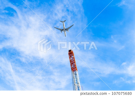 Passenger plane flying low in the blue sky and crane at construction site B-2 High chroma contrast Passenger plane flying low in the blue sky and crane at construction site B-2 High chroma contrast 107075680