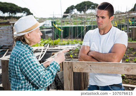Elderly woman and young man talking on the border of the garden plot 107076615