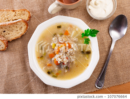 Popular dish of Russian cuisine is pickle soup with meat, cooked on basis of pickled cucumbers and pearl barley or rice, decorated with sprig of parsley 107076664