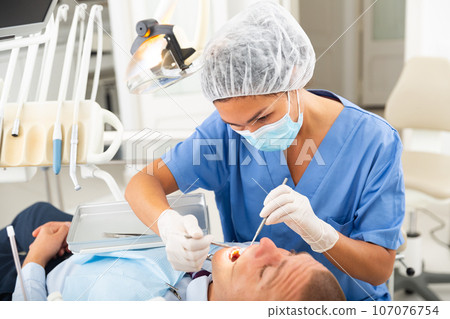 Dentist is treating male patient which is sitting in dental chair 107076754