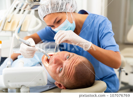 Qualified woman dentist in a protective mask treats a man patient Qualified woman dentist in a protective mask treats a man patient 107076769