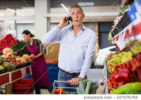 Man talking on cellphone while buying vegetables and fruits at market 107076798