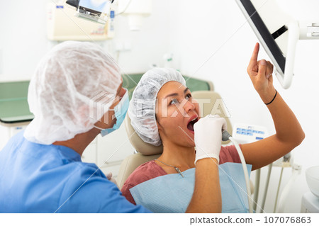 Qualified man dentist conducts an examination of a woman patient using an apexlocator 107076863