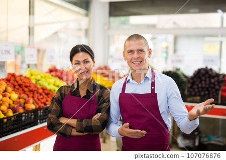 Successful couple of greengrocery owners offering fruits and vegetables Successful couple of greengrocery owners offering fruits and vegetables 107076876