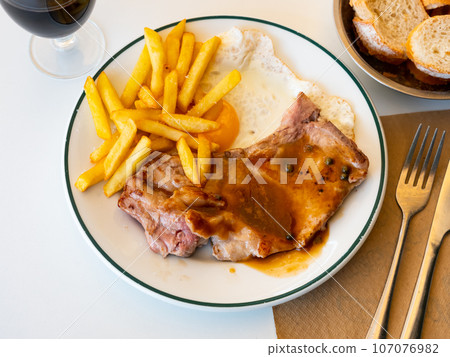 Close up of grilled pork with french fries and egg served on plate. Traditional spanish dish Cerdo patata eggs 107076982