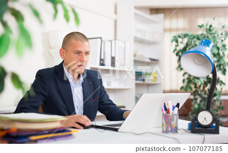 Focused young man working on laptop at office desk 107077185