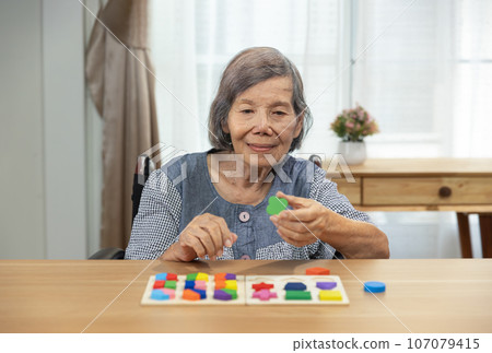 Senior woman playing wooden shape puzzles game for dementia prevention 107079415