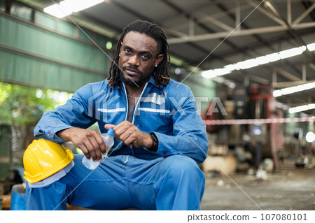 Man African American engineer holding plastic bottle drinking water after working at factory. Man African American engineer holding plastic bottle drinking water after working at factory. 107080101