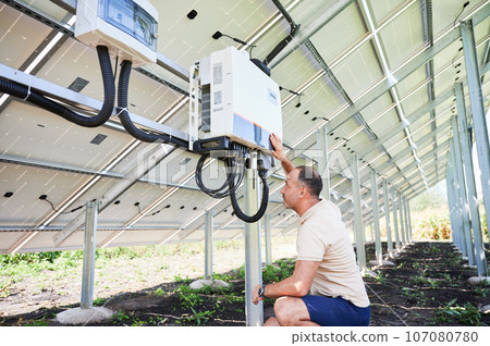 Male worker checking if solar inverter working right. Young man configuring inverter. Back view of photovoltaic battery. 107080780