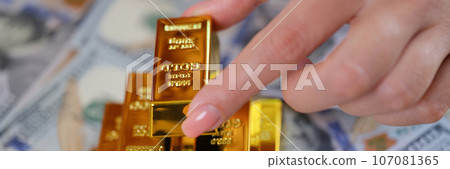 Human hand arranging pile of gold bars on US dollars banknotes. 107081365