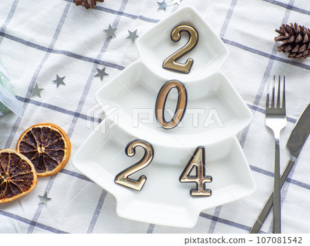 Empty christmas tree shaped white plate with 2024 on towel background Empty christmas tree shaped white plate with 2024 on towel background 107081542