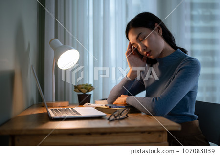 A tired Asian female college student is falling asleep at a table in her room in the evening. 107083039
