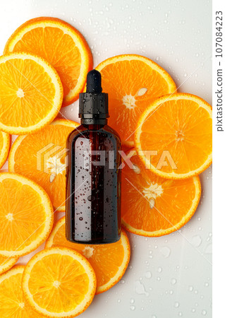 Glass bottle of essential citrus oil on oranges background 107084223