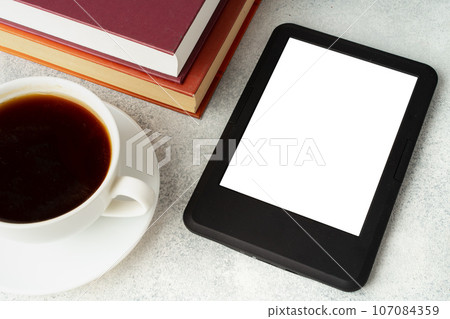 Composition with modern e-book reader, hardcover book and cup of coffee on table Composition with modern e-book reader, hardcover book and cup of coffee on table 107084359