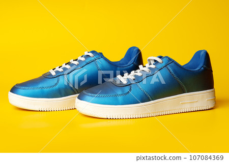 Blue new sneakers on yellow studio background Blue new sneakers on yellow studio background 107084369