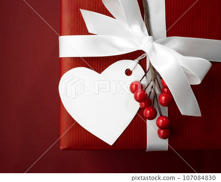 Empty white heart-shaped gift tag on a red gift box with a white ribbon. Space for your text. Valentine's Day Card 107084830