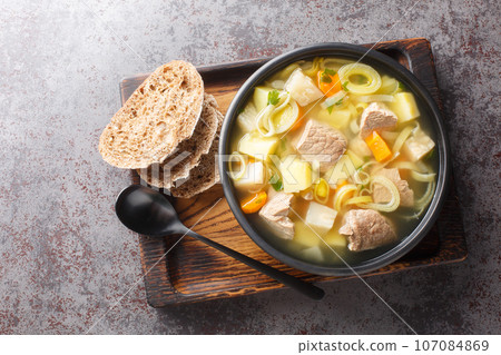 Kottsoppa soup with boiled meat, chopped carrots, onions, parsnip, celery and leeks close-up on a plate. Horizontal top view Kottsoppa soup with boiled meat, chopped carrots, onions, parsnip, celery and leeks close-up on a plate. Horizontal top view 107084869