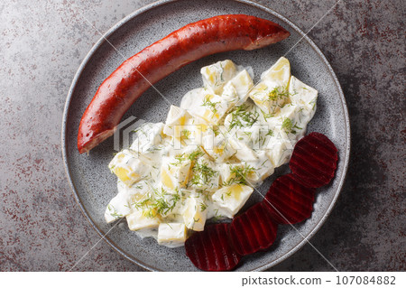 Smoked sausage with potatoes in cream sauce with dill and boiled beets close-up on a plate. Horizontal top view Smoked sausage with potatoes in cream sauce with dill and boiled beets close-up on a plate. Horizontal top view 107084882