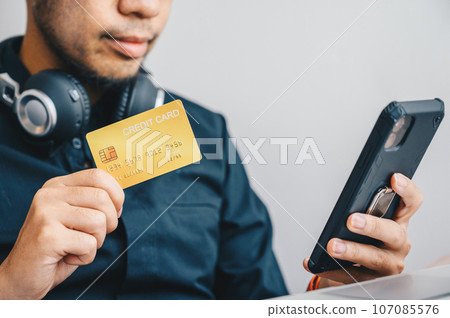 Close-up of businessman holding gold credit card for payment online shopping on smartphone. Credit card lets cardholders borrow funds with which to pay for goods and services depend on the condition. Close-up of businessman holding gold credit card for payment online shopping on smartphone. Credit card lets cardholders borrow funds with which to pay for goods and services depend on the condition. 107085576