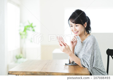 一個年輕的女人，在客廳裡操作智能手機 107086493