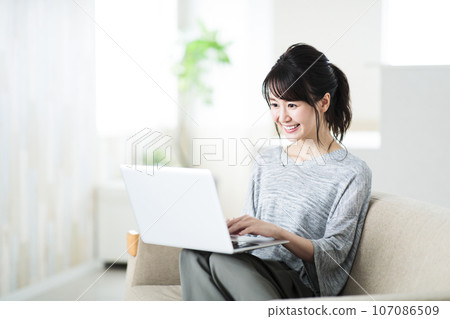 Young woman sitting on the sofa in the living room and operating a computer Young woman sitting on the sofa in the living room and operating a computer 107086509
