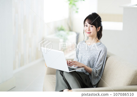 Young woman sitting on the sofa in the living room and operating a computer Young woman sitting on the sofa in the living room and operating a computer 107086510
