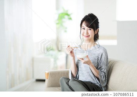 Young woman eating yogurt in the living room Young woman eating yogurt in the living room 107086511