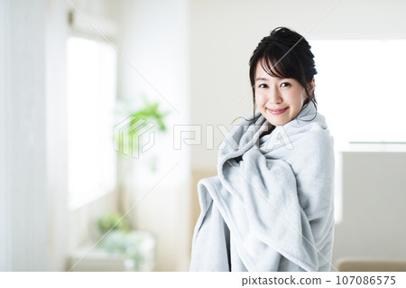 Young woman wearing a blanket in the living room Young woman wearing a blanket in the living room 107086575