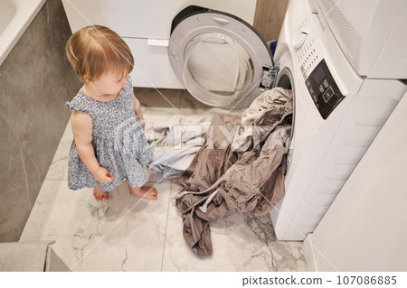 House cleaning and change of bed linen. Happy baby girl one and a half, helper are having fun and smiling while in a bright apartment. Helps parents change bed linen and do laundry in the washing 107086885
