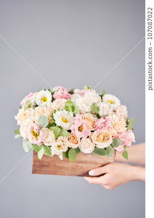 Florist woman creates flower arrangement in a wooden box. Beautiful bouquet of mixed flowers. Floral shop concept . Handsome fresh bunch. Flowers delivery 107087022