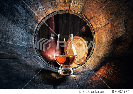 A glass of whiskey in oak barrel 107087575