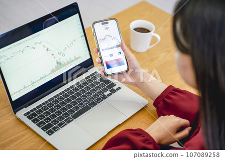 一位女性邊看智慧型手機邊投資 107089258