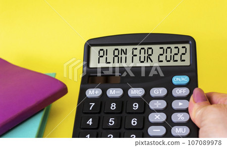 Plan for 2022 on display of a calculator in a woman's hand on a yellow background. Plan for 2022 on display of a calculator in a woman's hand on a yellow background. 107089978