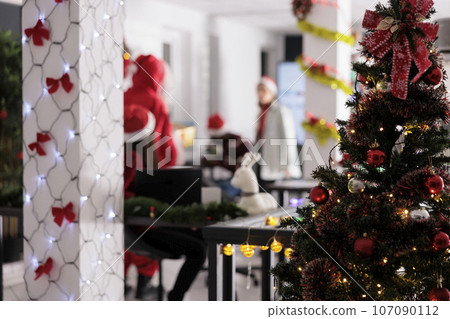 Festively ornate Christmas tree close up with businessmen working in blurry background. Modern office with pretty xmas lights decking the halls during winter holiday season 107090112